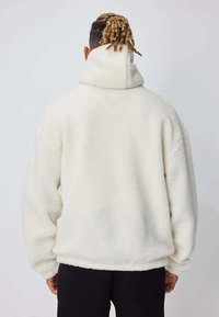 Pull-over en polaire blanche avec un col haut et une coupe oversize. Tissu texturé avec une apparence douce et pelucheuse ; poignets et ourlet côtelés.