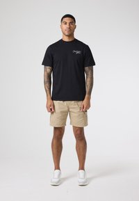 Czarna bawełniana koszulka z krótkim rękawem, z małym białym logo. Połączona z beżowymi szortami cargo i białymi sneakersami. Prosty design.