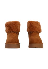 Bottines en suède marron avec un revers en fourrure marron duveteuse, semelle en caoutchouc plate et détails de couture sur le côté.