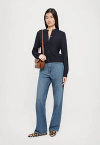 Tumesinine kootud kardigan püstise kraega, nupuvajutusega, sobitatud helesiniste laia lõikega teksade ja leopardimustriliste lapikutega. Pruun õlakott.