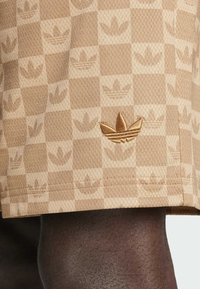 Tan athletic shorts with a textured, checkerboard pattern featuring subtle logo designs. Embroidered logo in matching color on the hem.