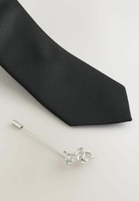 Melna satīna kakla saite ar smailu galu, kas apvienota ar sudraba ziedu kakla pinumu, kam ir caurspīdīgi dekori un elegants dizains.