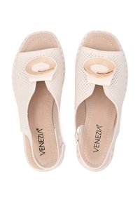 Perforierte beige Rutschen-Sandalen mit einem auffälligen kreisförmigen Akzent in Goldton an der Vorderseite und einer strukturierten Innensohle.