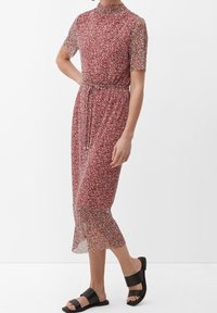 Červené midi šaty s květinovým vzorem, průhledné, s krátkými rukávy a páskem v oblasti pasu, zakončené rozšířeným spodním lemem. V kombinaci s černými sandály.