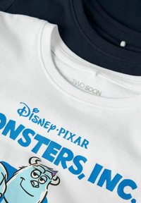 Divas divi kokvilnas T-krekli viens uz otra; augšējais balts ar zilu "Disney Pixar Monsters, Inc." druku, uz kura attēlots zils monstru ilustrācija; apakšējais tumši zils.