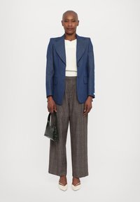 Blue tailored blazer over a white knit top, paired with plaid wide-leg trousers and cream pointy-toed heels. A dark green handbag is held.