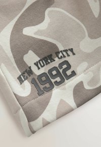 Beige camouflage sweatshirt met zwart rubberachtig tekst: "NEW YORK CITY" en "1992," met textuur detail.