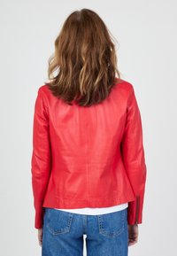 Červená kožená bunda s přiléhavým střihem, hladkou texturou a zipovými manžetami, zkombinovaná s modrými džíny, pohled zezadu.