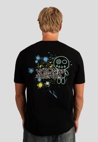Zwarte katoenen T-shirt met een grafisch ontwerp op de achterkant met de tekst "VERKEERDE VRIENDEN" en kleurrijke spetterpatronen. Standaard pasvorm.