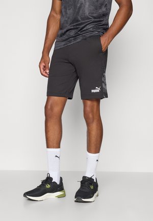 Bermude atletice negre dintr-un material ușor, cu un model de camuflaj pe lateral și logo-ul alb Puma. Asortate cu încălțăminte neagră și șosete albe.