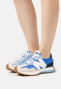 Modré a šedé tenisky s texturovaným svrškem; mají semišové a síťované materiály, gumovou podrážku a výrazné logo "N".