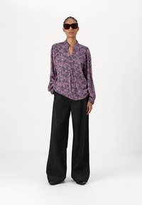 Purple blouse with floral pattern, long sleeves, and a button-down front, paired with black wide-leg trousers and dark sunglasses.