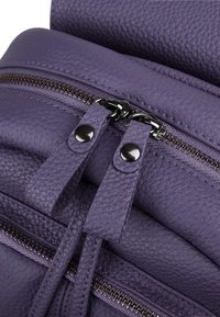 Sac à dos en cuir texturé violet avec double zipp, matériel noir, couture détaillée et sangles lisses. Design compact et fonctionnel.