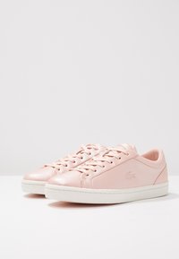 Baskets en cuir rose clair avec semelle en caoutchouc blanche, bout arrondi et lacets. Logo Lacoste embossé sur le côté, texture lisse.
