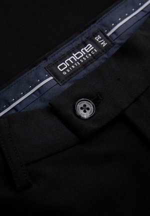 Pantalons formels noirs en tissu lisse, avec fermeture à bouton et une étiquette portant la mention "ombre quintessence". La doublure intérieure présente un motif en chevrons.