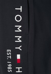 Marineblaue Stoff mit weißem, gesticktem Text "TOMMY" und "EST. 1985", mit einem kleinen rot-weiß-blauen Logoakzent. Weiche Textur.