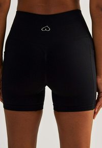 Black high-waisted shorts featuring a ribbed texture, side pockets, and a small white heart logo at the center back waistband.