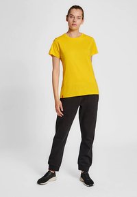 Gul bomullst-shirt med korta ärmar, rak passform; kombinerad med svarta mjukisbyxor med avslappnad skärning och elastiska muddar.