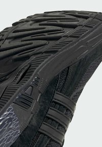 Black athletic shoe sole featuring textured rubber, grooves for traction, and smooth plastic accents; combines suede and mesh materials.