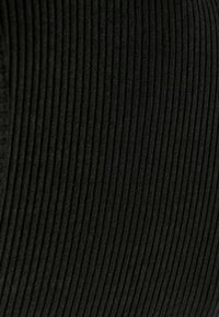 Gros plan sur un tissu noir côtelé avec des lignes texturées verticales et des détails de couture visibles.