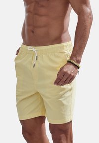 Yellow swim shorts with an elastic waistband, drawstring closure, and side pockets. Fabric appears lightweight and smooth.