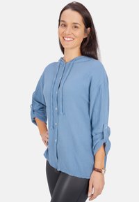 Blaue Kapuzenbluse aus strukturiertem Stoff, mit Knopfleiste, hochkrempelbaren Ärmeln und lässiger Passform.