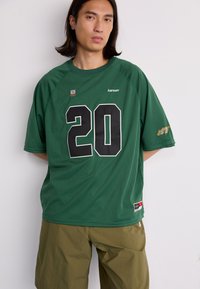 Green mesh athletic jersey with black number 20, logo on the chest, and additional graphics on the sleeve. Short sleeves and loose fit.