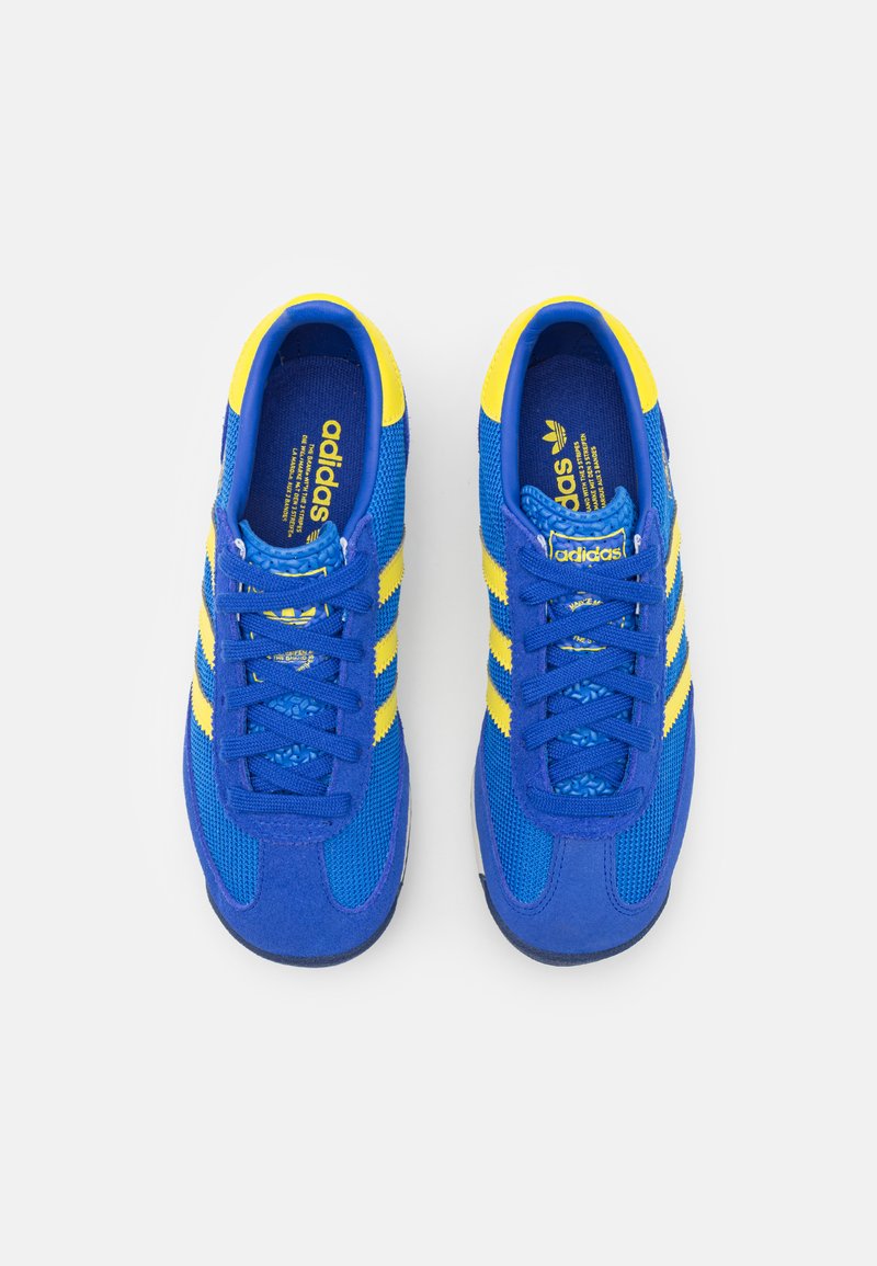 Zapatillas deportivas azules con acentos amarillos, materiales de malla y ante, puntera redonda, seis ojales y tres rayas laterales.