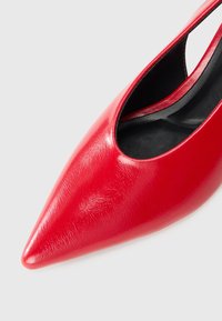 Chaussure à talon aigu rouge avec bout pointu, en cuir brillant, présentant un design découpé sur le côté et une doublure intérieure lisse noire.