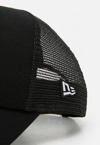 Svart caps med mesh-sidelapper, strukturert design, og en hvit brodert logo foran. Stoffet er glatt med en teksturert mesh.