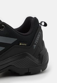 Schwarzer Wanderschuh mit strukturiertem Obermaterial, reflektierenden grauen Akzenten und einer robusten Laufsohle. Mit GORE-TEX-Logo und Zuglasche für einfaches Anziehen.