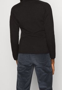 Svart stickad jacka med långa ärmar och en figurnära design, ihop med mörkblå corduroybyxor med bakfickor och strukturerad tyg.