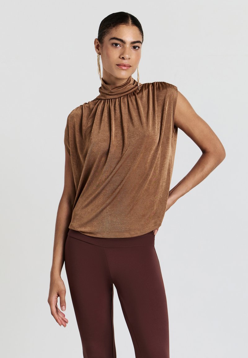 Haut sans manches en bronze avec col roulé froncé, design drapé, texture lisse, associé à des leggings bordeaux ajustés.
