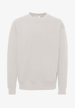 Svijetlosiva majica s okruglim izrezom izrađena od mekog materijala. Ima rebraste manžete i donji rub, a lijeva rukava ukrašena je oznakom i malim logotipom.