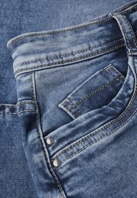 Jeans i ljusblå denim med urtvättad textur, med gula sömmar, en framficka och metalldetaljer.