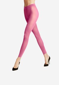 Leggings rosa brillante con una texture trasparente, design aderente e lunghezza alla caviglia, abbinati a tacchi alti neri.
