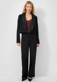 Blazer noir court avec revers en satin, associé à un pantalon large noir et un top bordeaux. Texture lisse et coupe ajustée.