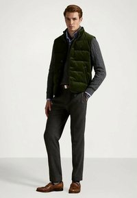 Roheline puhvipaljakas halli kaelus-sokiga sviitri kohal, kombineeritud hallide ruuduliste püksidega ja pruunide nahakingadega. Mudel seisab neutraalses taustas.