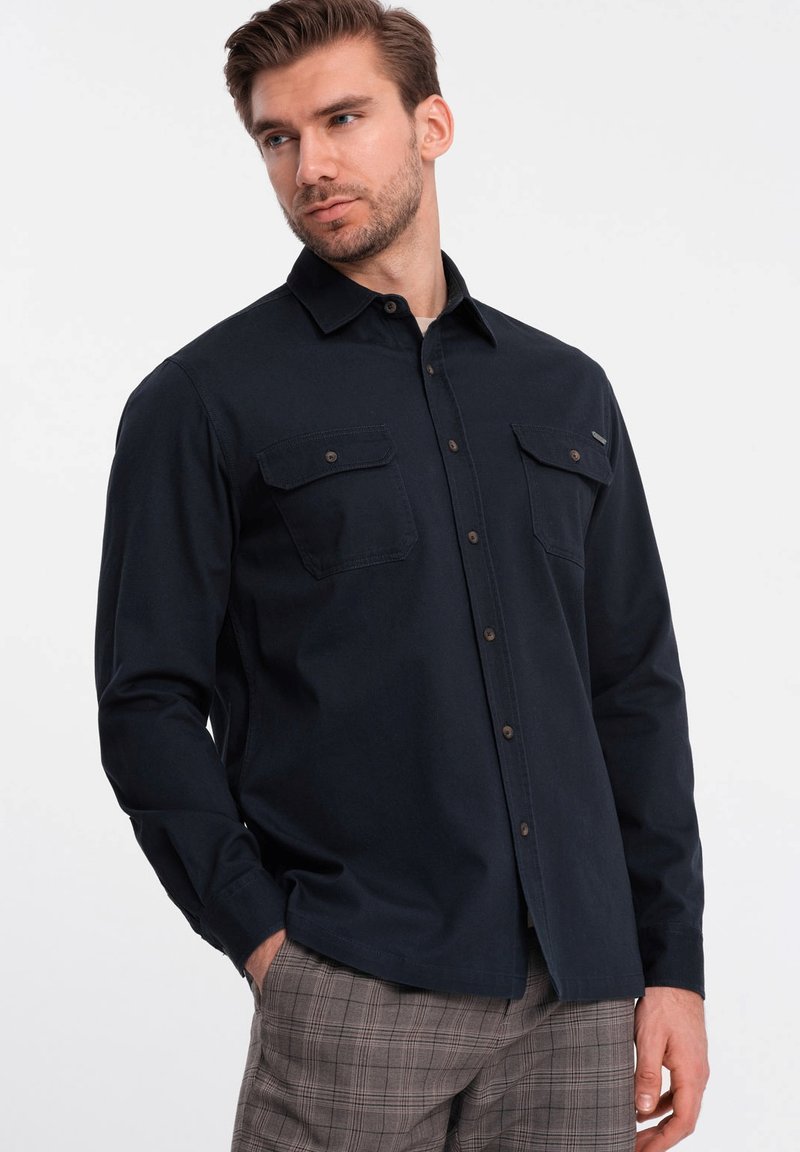 Camicia blu navy a maniche lunghe con chiusura a bottoni, due tasche sul petto e colletto. Realizzata in tessuto morbido con una vestibilità aderente.