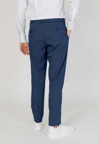 Pantalone s mornarskim prugama u tapered kroju, s stražnjim džepovima na dugmad. Upareni s bijelim tenisicama za ležeran izgled.