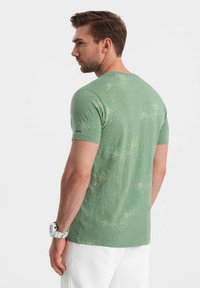 Vihreä lyhythihainen t-paita, jossa on teksturoitu kuvio, pyöreä pääntie ja pieni logo yksityiskohtana hihassa.