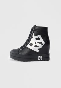 Crne wedge tenisice s debelim platformom, vezanjem sprijeda i velikim bijelim DKNY logotipom sa strane i na potplatu.