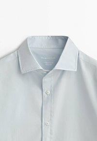 Camicia di cotone azzurro chiaro con colletto classico, chiusura a bottoni e dettagli di cuciture sottili. Texture liscia e design minimale.