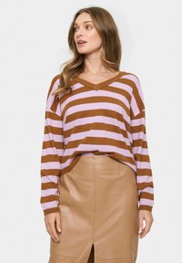 Maglione a righe marroni e lilla con scollatura a V, abbinato a una gonna in pelle beige aderente con una fessura frontale e una texture liscia.