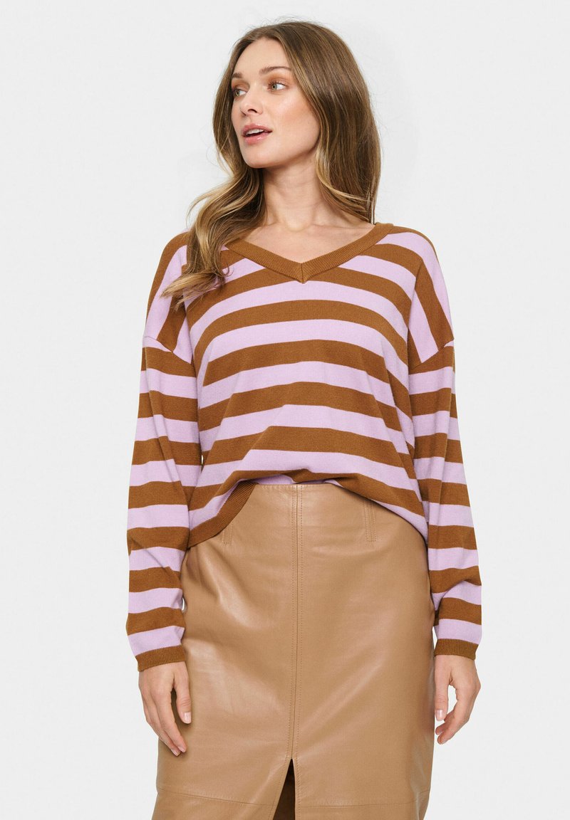 Maglione a righe marroni e lilla con scollatura a V, abbinato a una gonna in pelle beige aderente con una fessura frontale e una texture liscia.