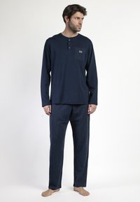 Camisa de manga larga azul marino con una tapeta de botones y un bolsillo a rayas, combinada con pantalones a rayas finas. Textura suave y corte relajado.