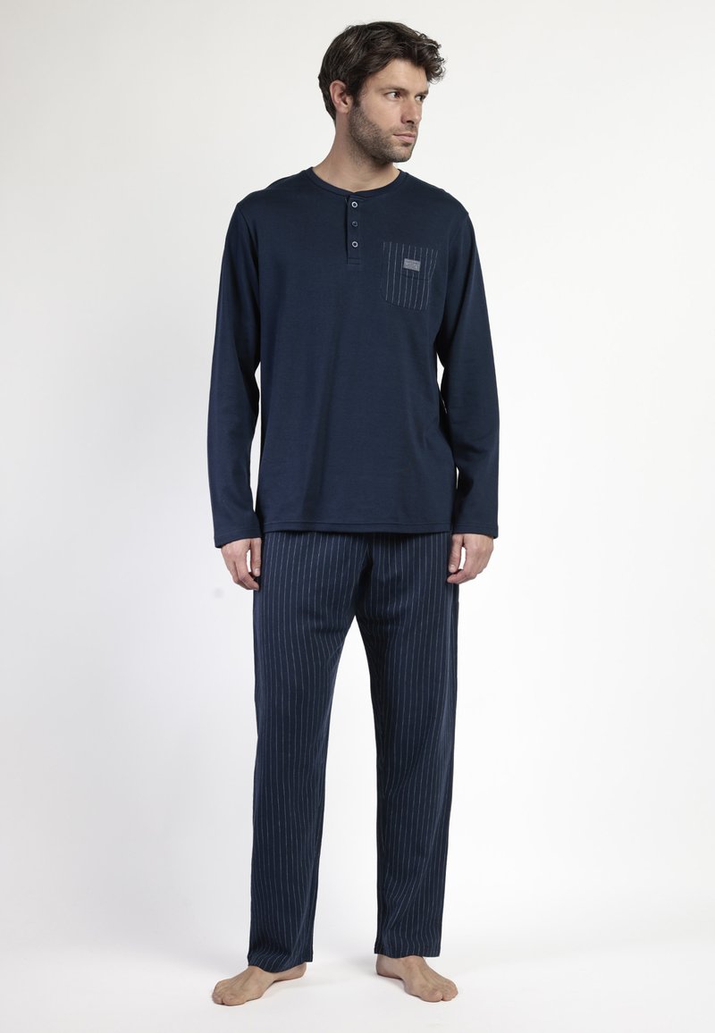 Camisa de manga larga azul marino con una tapeta de botones y un bolsillo a rayas, combinada con pantalones a rayas finas. Textura suave y corte relajado.