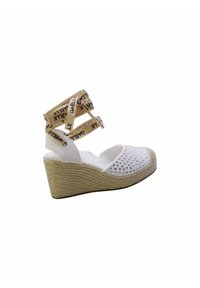 Sandalo bianco con zeppa, dotato di suola in juta intrecciata, dettagli con borchie sulla parte superiore e cinturini beige con marchio stampato.