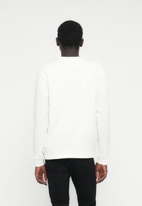 Weißes Sweatshirt mit Rundhalsausschnitt und langen Ärmeln, mit gerippten Bündchen und Saum, kombiniert mit schwarzen Jeans. Strukturierter Stoff sichtbar.