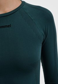 Langdurige sporttop met lange mouwen in donker teal, gemaakt van rekbaar materiaal. Heeft ademende meshdetails en een ronde halslijn met logo.